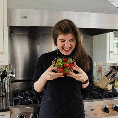 A woman stands in her kitchen, holding a bowl of vibrant strawberries, showcasing her fresh ingredients for a meal.