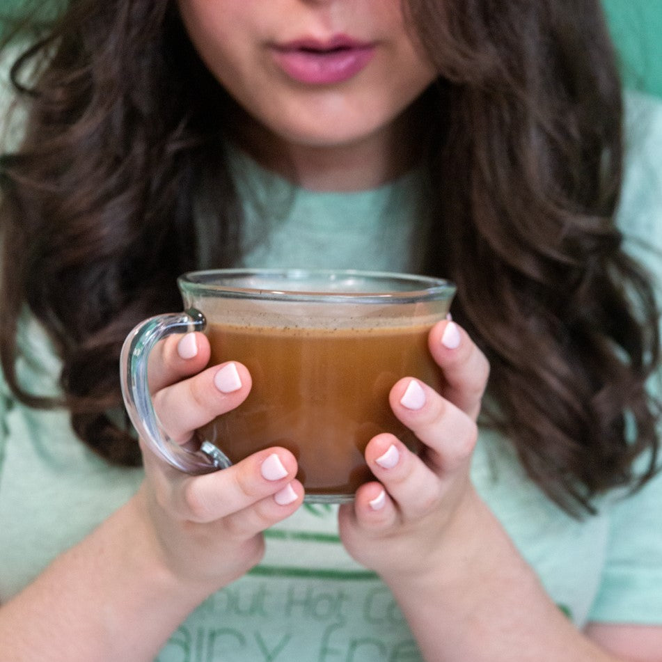 Person holding a clear glass mug of Bare Life coconut hot cocoa in both hands
