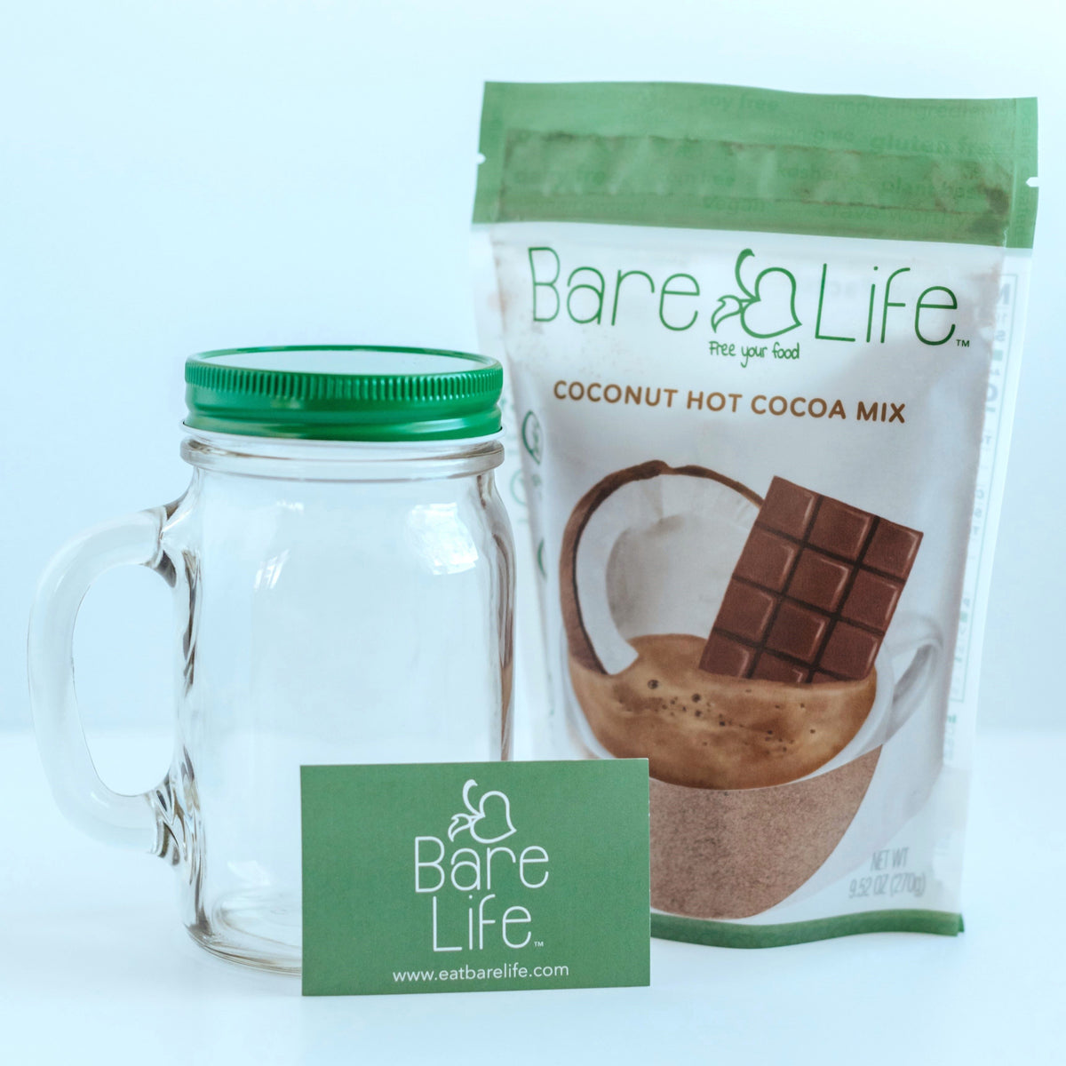 Bare Life glass mason jar with green lid beside a coconut hot cocoa pouch and Bare Life card