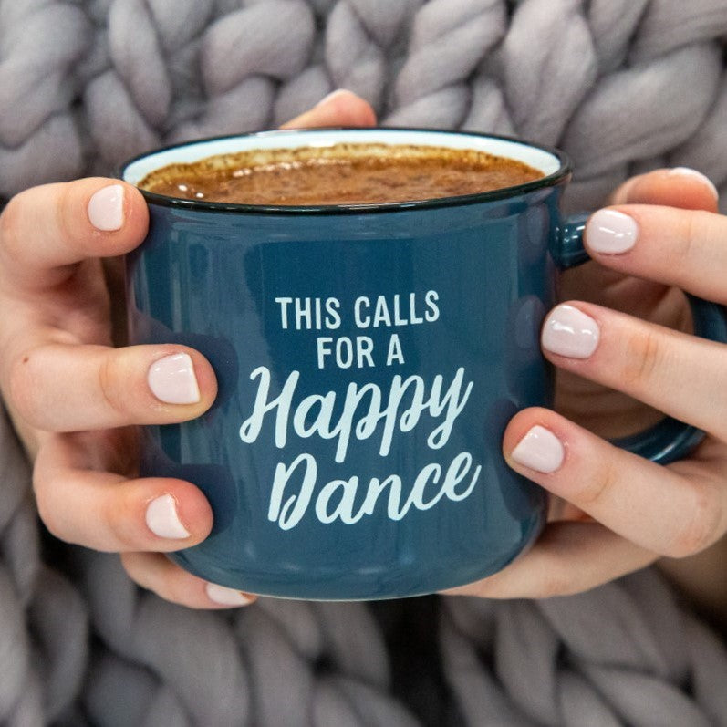 Hands holding a blue mug of hot cocoa reading This Calls for a Happy Dance against a chunky knit blanket