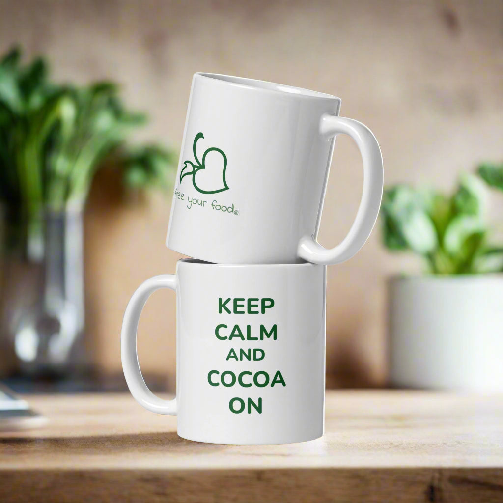 Two stacked white Bare Life mugs showing the Keep Calm and Cocoa On lettering and Free Your Food logo