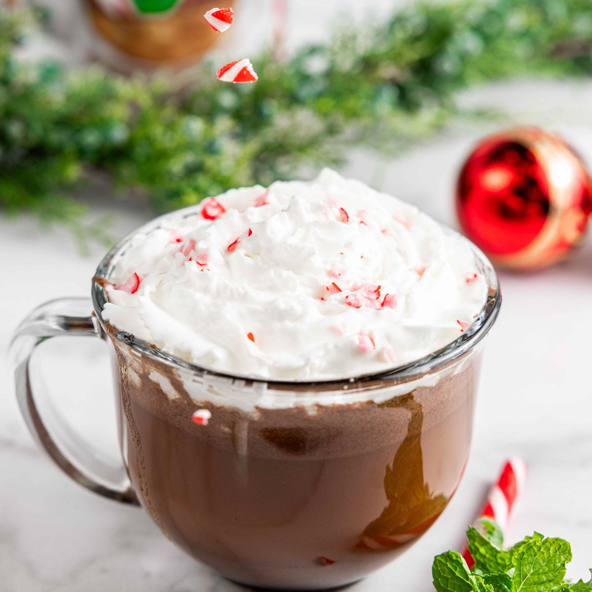 Glass mug of Bare Life peppermint hot cocoa topped with whipped topping and crushed candy canes